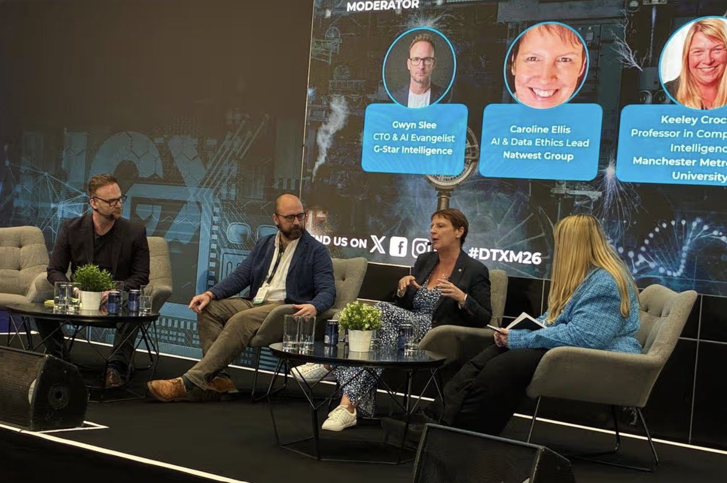 Gwyn Slee moderating the Progress at a Price panel on the main stage at DTX Manchester 2026, with the panellists and the event screen behind
